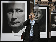 Мужчина пьет напиток на фоне фотографий Владимира Путина и российских спортсменов Мужчина пьет напиток на фоне фотографий Владимира Путина и российских спортсменов