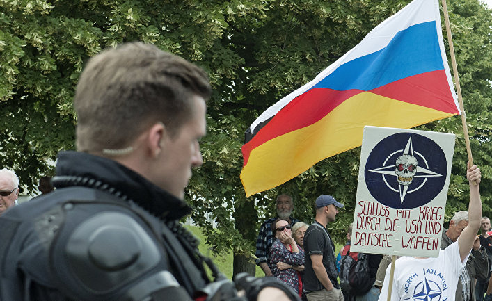 Митингующий держит в руках выдуманный Русско-Германский флаг на митинге против мигрантов