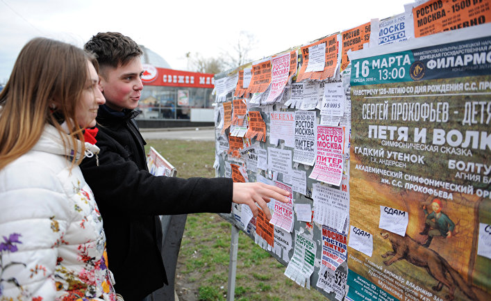 Юные жители города читают объявления на уличном стенде в Донецке