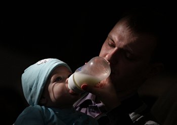 Отец кормит ребенка из из бутылочки на фестивале BabyFest в Сокольниках Отец кормит ребенка из из бутылочки на фестивале BabyFest в Сокольниках