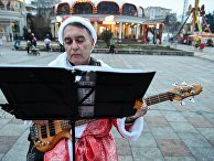 Музыкант в костюме Деда Мороза выступает на набережной в Ялте, Крым Музыкант в костюме Деда Мороза выступает на набережной в Ялте, Крым