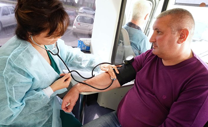 Медик измеряет давление мужчине в мобильном пункте вакцинации в Калининграде